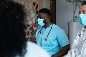 Diverse male and female doctors wearing face masks sitting in hospital corridor having discussion / Photodune, Misc