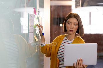 Asian businesswoman standing in front of whiteboard and writing holding laptop having video call / Photodune, Misc