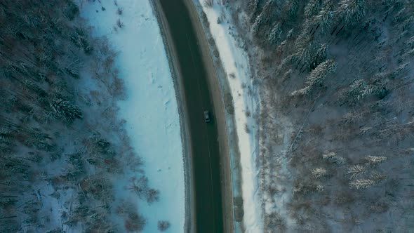 Aerial View of a Car Driving on a Snowy Road in a Winter Forest