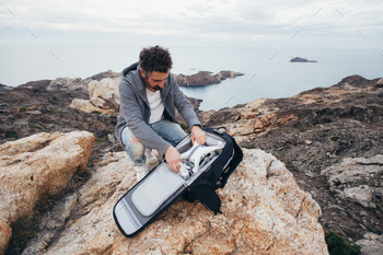 nturer and location explorer, traveler unpacks backpack with expensive equipment and drone, ready to fly over oceanside and inspiring scenery