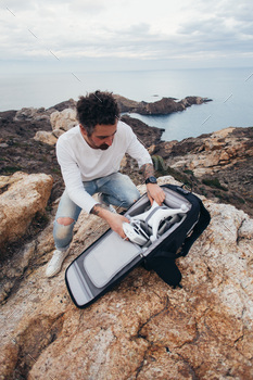 nturer and location explorer, traveler unpacks backpack with expensive equipment and drone, ready to fly over oceanside and inspiring scenery