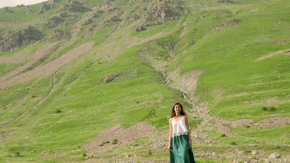 Beautiful woman standing in a grassy meadow beneath a large rocky mountain in Barcelonnette, France.