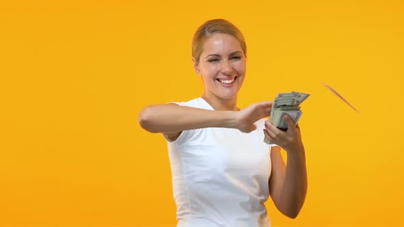 Extremely Happy Woman Throwing Dollars Against Orange Background, Lottery Winner