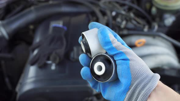 master in glove holds lever silent block in his hand against background engine.