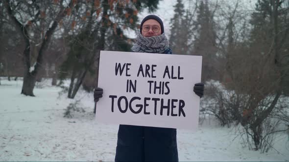 A Male Protester in a winter park Holding a banner We Are All in This Together