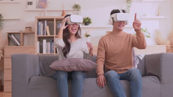 Asian couple playing game and having fun together with virtual reality headset on the sofa.