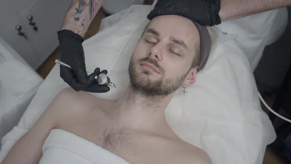 Top View of Young Handsome Man Lying in Beauty Parlor As Unrecognizable Beauty Therapist Hydrating