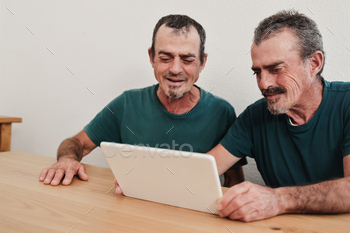 Senior twin men using digital tablet together at home - Focus on right face