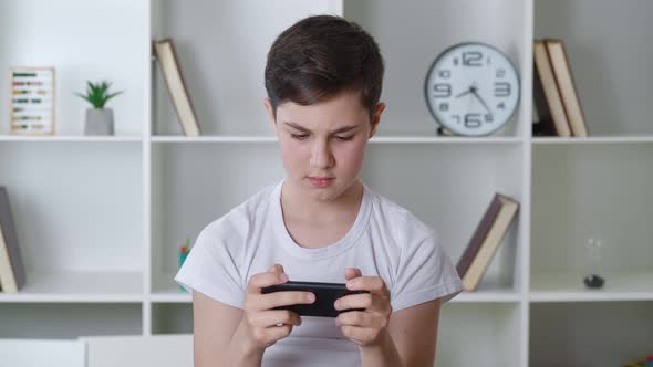 Handsome Boy 13 Years Old Playing Mobile Game on Smartphone at Home