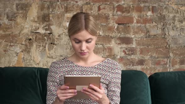 Woman sits on sofa, she's using a tablet computer. Woman touching Digital Tablet at home.