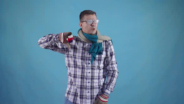 Distressed Frozen Man Covered with Frost in Gloves and Scarf on Blue Background Shows Finger Down