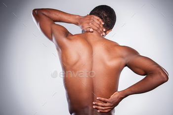 n man touching his neck and hip while standing against grey background