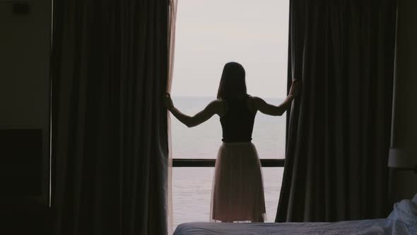 Back View Young Happy Woman Closing Window Curtains with Epic Sea View, Walks Back To Dark Hotel