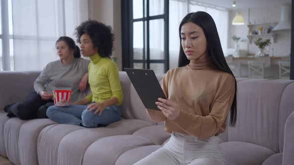 Confident Serious Asian Beautiful Woman Examining Documents Sitting on Couch in Home Office with