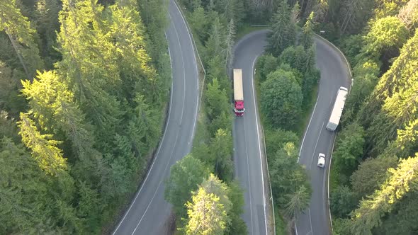 Aerial view of winding road with mowing cars and trucks in high mountain pass trough dense woods.