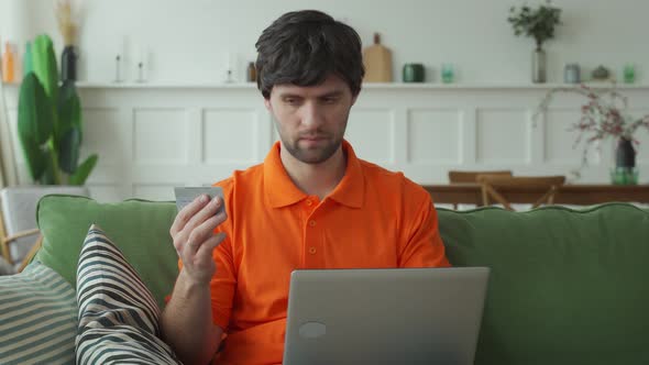 Man Sitting on Couch in Living Room with Laptop and Credit Card