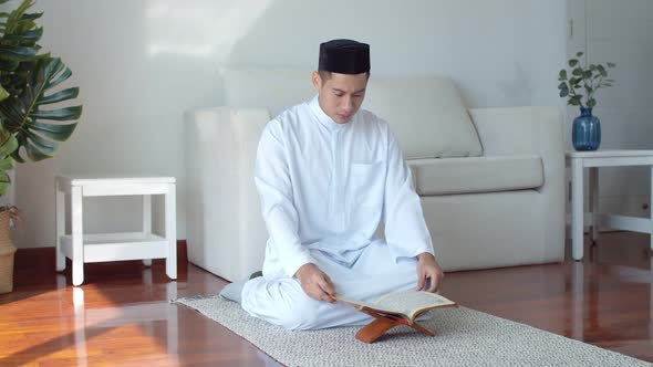 Young Muslim man wearing Islamic clothes reading the Quran