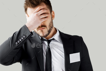 ear covering face with hand while standing against grey background