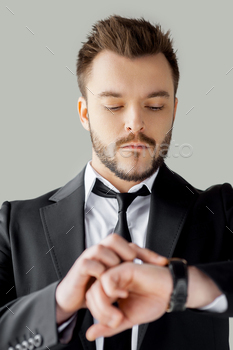 n formalwear checking the time while standing against grey background