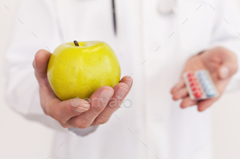 rm holding an apple in one hand and pills in another one while standing isolated on white