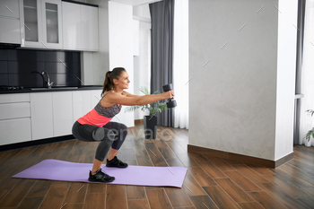 Smiling woman training at home using dumbbell / Photodune