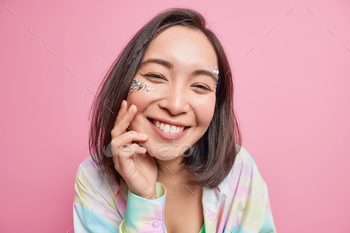 Portrait of good looking charming Asian woman smiles gently enjoys freshness of skin wears stones on / Photodune