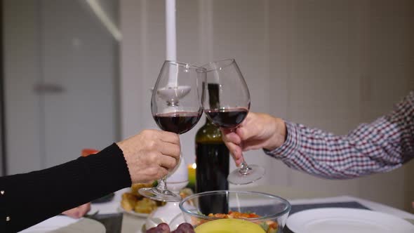 Close Up of Clinking Red Wine Glasses During Romantic Dinner. Happy Cheerful Senior Elderly Couple