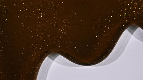 Brown Cosmetic Gel Fluid Gold Interspersed Flowing with Down on a White Surface