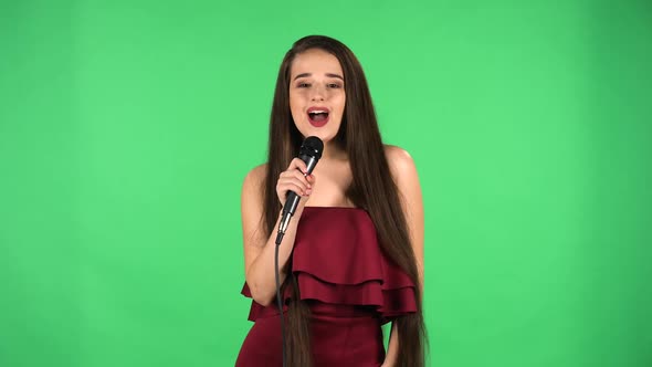 Portrait of Beautiful Young Woman Coquettishly Looking at Camera and Sings Song Into Microphone