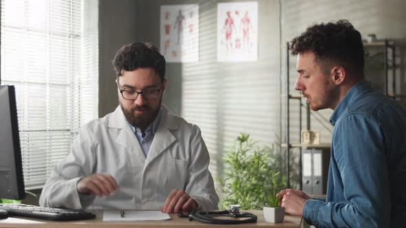 Male Physician Showing Computer to Young Male Patient During Consultation in a Health Clinic