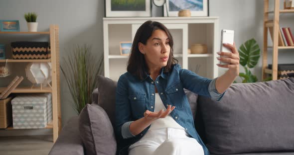 Angry Young Lady Talking on Smartphone Making Video Call Gesturing at Home