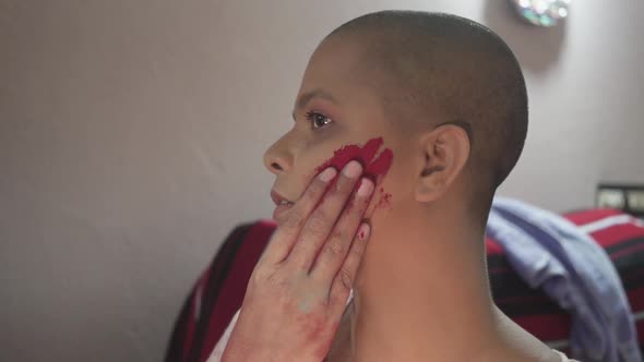 Bald Cancer patient Indian girl applies color powder on cheeks on Holi, Indian festival at home due