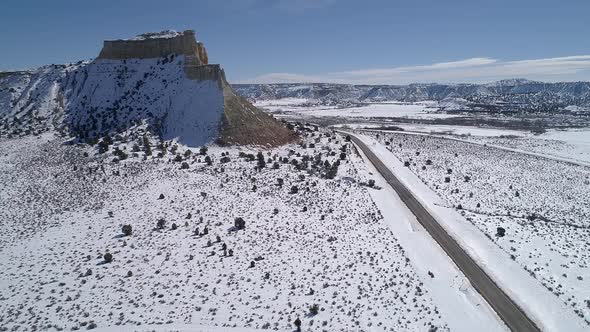 Flying over snow covered desert landscape past butte