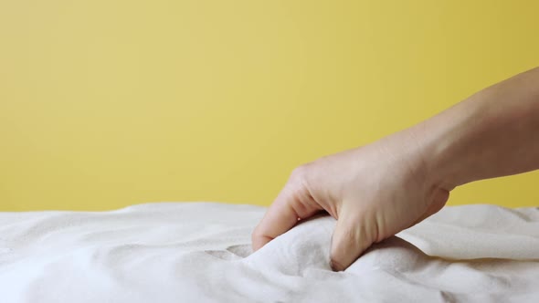 Woman's Hand Scoops Up and Sprinkles White Sand on Yellow Studio Background