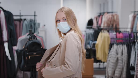 Millennial Woman in Face Medical Mask in Shopping Mall Chooses Autumn Jacket Coat New Outfit Trying