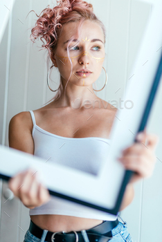 ooking aside, holding an empty picture frame, posing over light white background. Expressing feelings and emotions