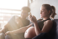 Future family. Pregnant woman is using her mobile phone. Copy space on the left side - PhotoDune Item for Sale