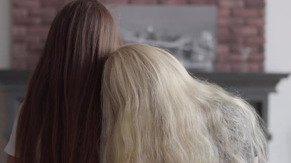 Back View of Two Girls with Long Beautiful Hair Sitting Near Each Other in the Living Room