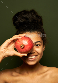  pomegranate fruit over her eye, posing isolated over green background. Healthy eating, vitamins concept
