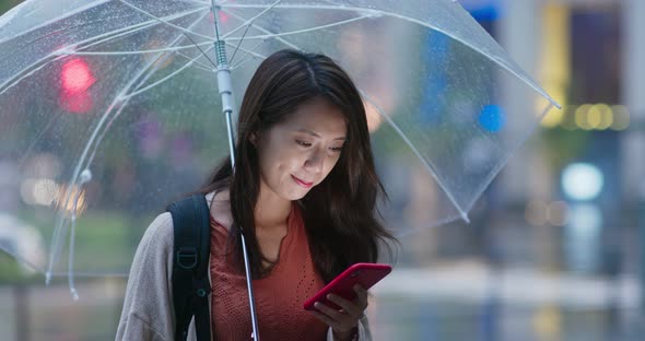 Woman use of mobile phone and hold with umbrella in the evening