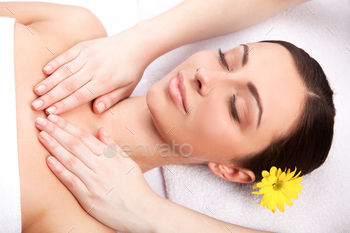 an with flower in head lying down and keeping eyes closed while massage therapist massaging her