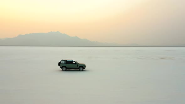 SUV Driving Through Bonneville Salt Flats With Vibrabnt Sunset In The Sky In Utah. - aerial