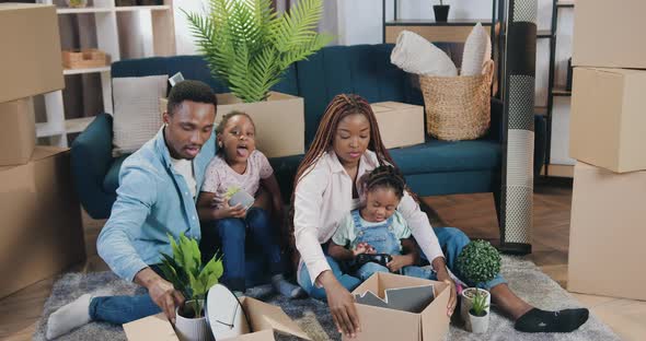 African American Couple with Kids Sitting on the Floor and Unpacking Boxes in Newly Acquired