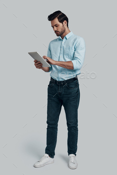 ng using digital tablet while standing against grey background