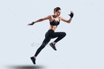 man in sports clothing jumping while hovering against grey background