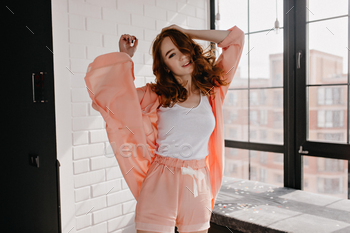Blissful woman in stylish pajama relaxing at home. Romantic ginger girl dancing in morning / Photodune