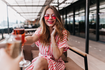 Good-looking young woman holding cocktail and smiling to camera in summer day. Ecstatic blonde girl / Photodune