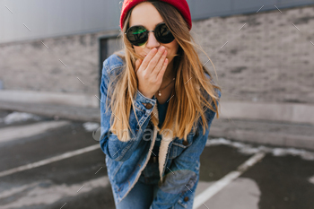 Winsome white girl in hat and sunglasses posing on urban background in spring day. Blonde woman in / Photodune