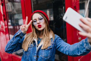 Lovely young woman with red lips making selfie in spring day and using phone. Outdoor portrait of e / Photodune