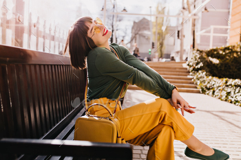 Glad laughing woman sitting on wooden bench in park. Outdoor photo of gorgeous young lady with brow / Photodune